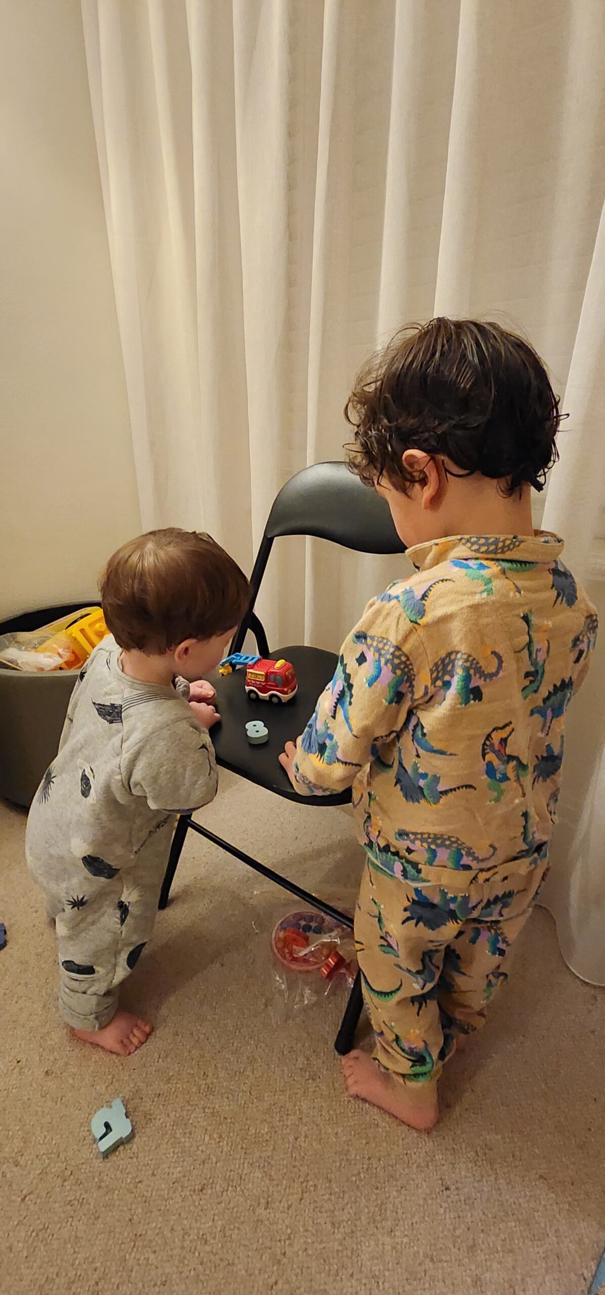 Two boys in pyjamas playing with toys on a foldable chair